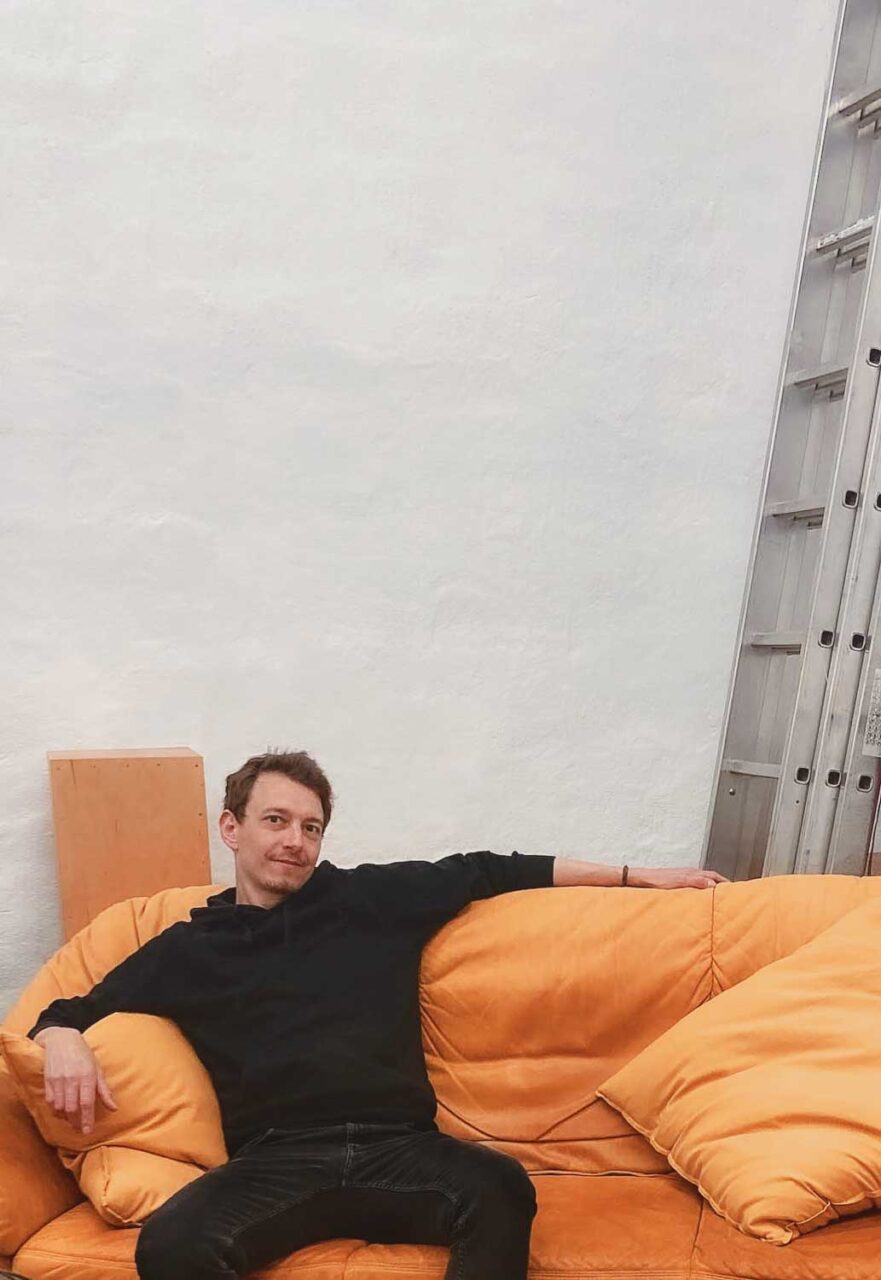 Christian Mirbach – Freelancer für Design und Marketing in Köln Ehrenfeld, auf einem Sofa sitzend